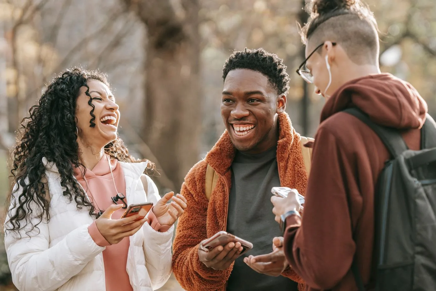 Three young friends laughing together outdoors while sharing something on a phone