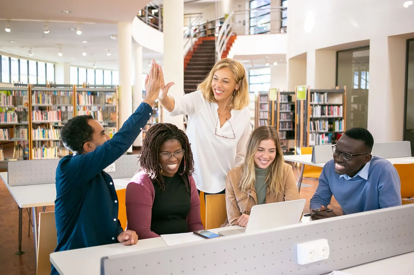 A group of students celebrating with a high five around a laptop in a library
